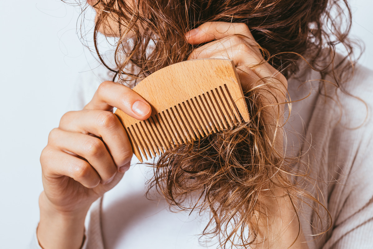 A young woman combing tangled ends of her curly hair with a wooden comb