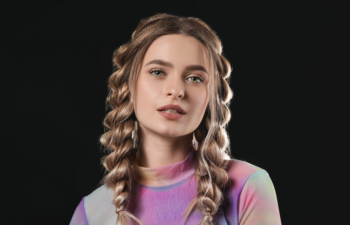 Beautiful young woman with braided hair on dark background