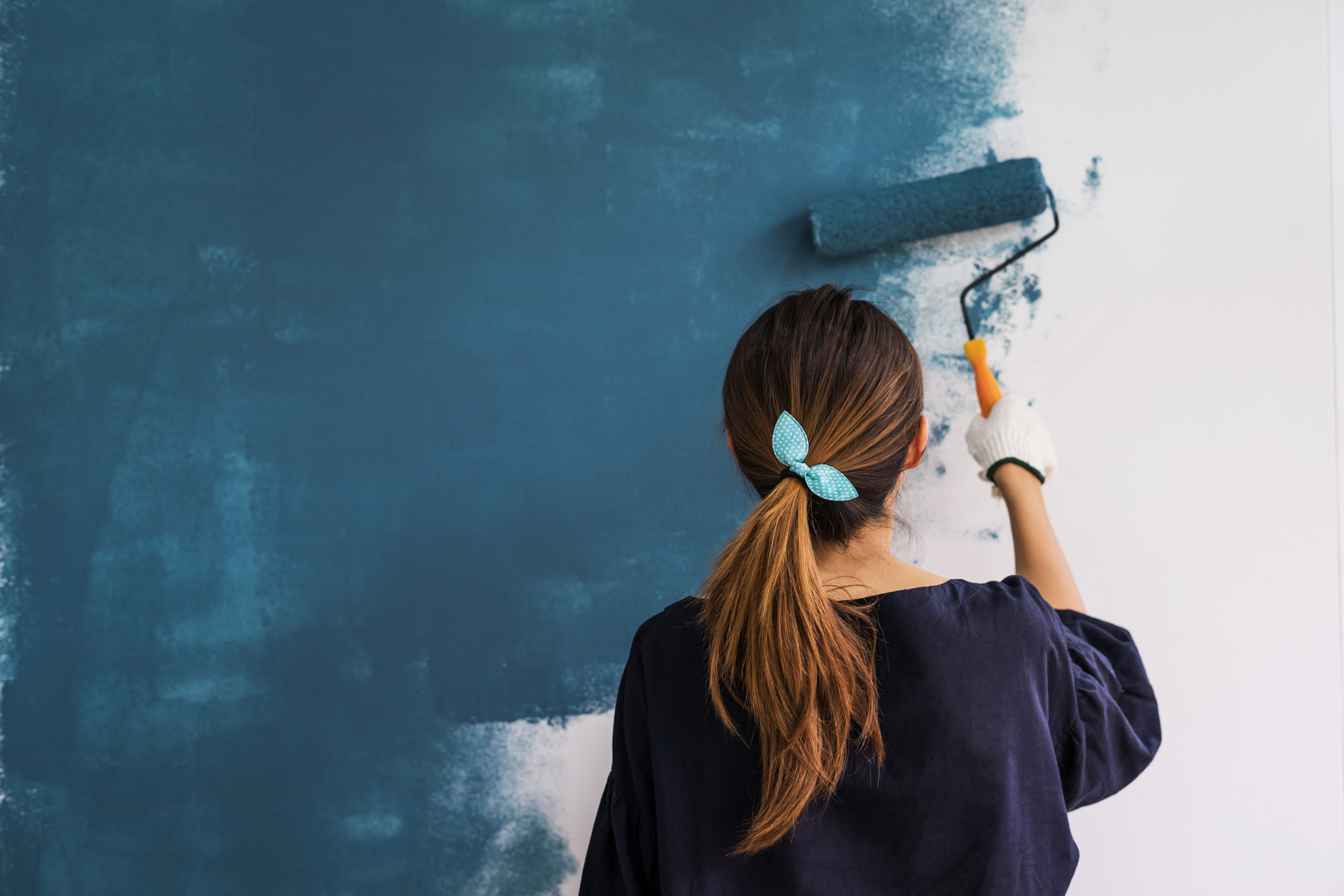 Girl with her hair tied behind her back and holding a paint roller