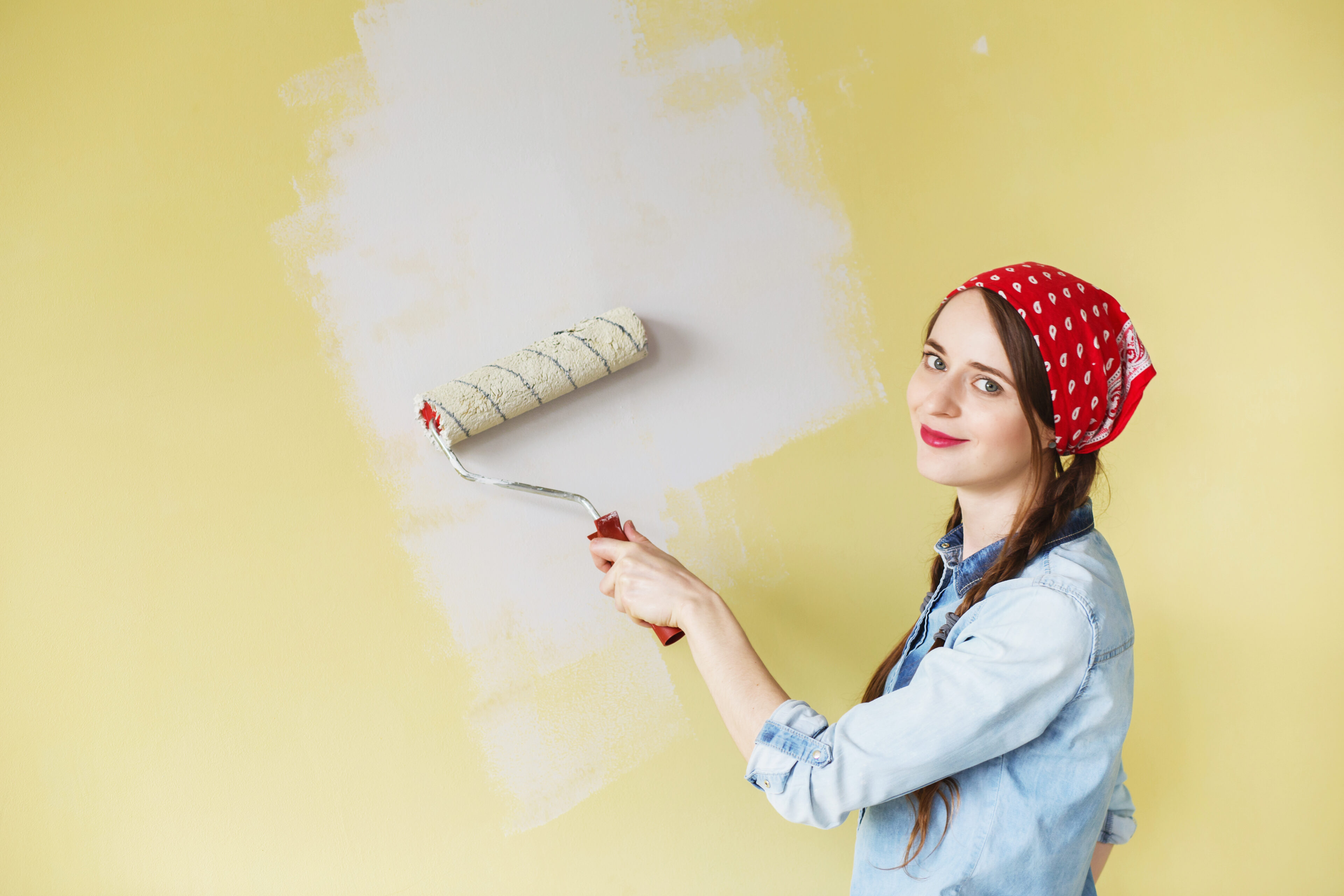Beautiful girl in red Headband painting the wall with paint roller