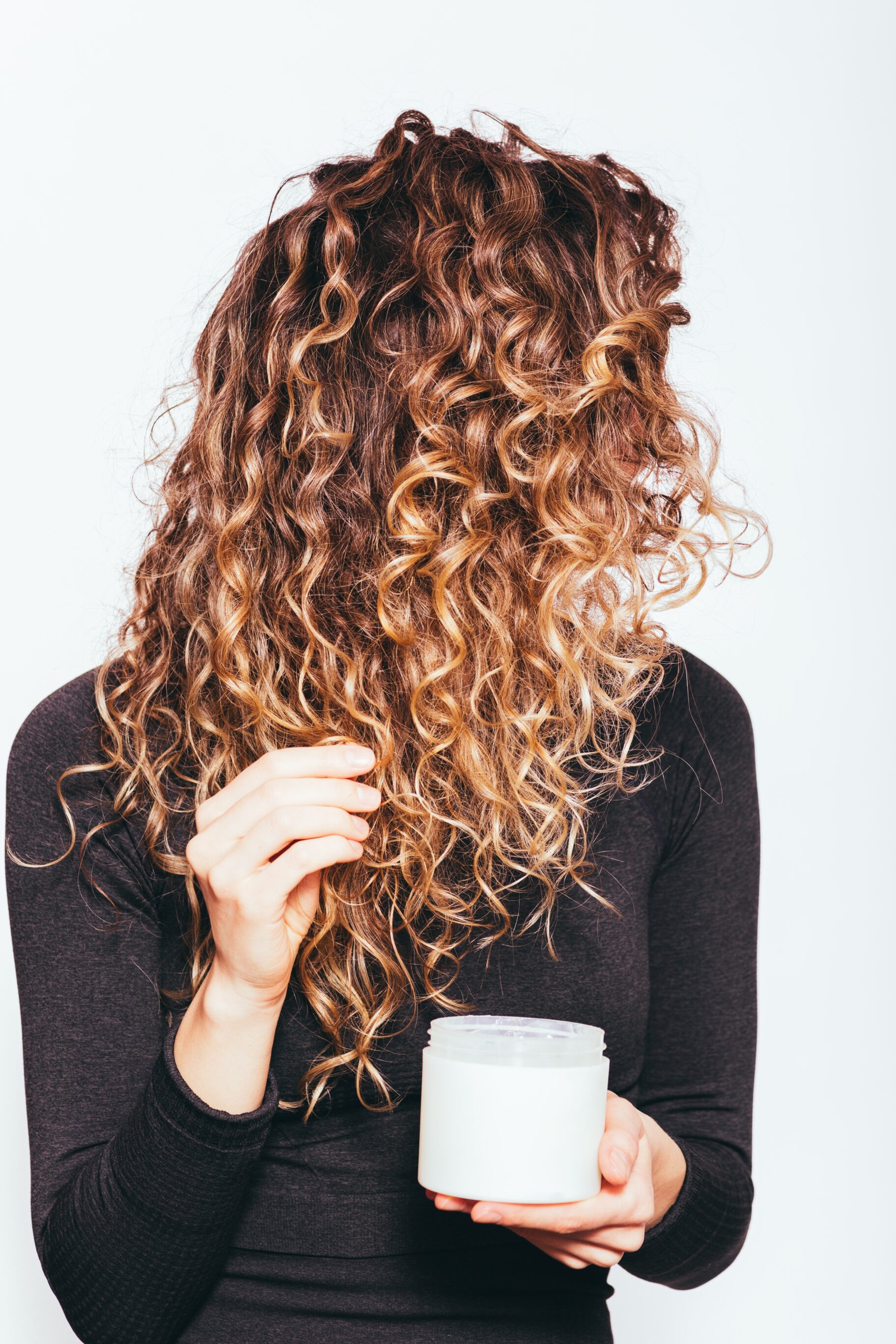 Young woman applying cosmetic cream to her long curly hair