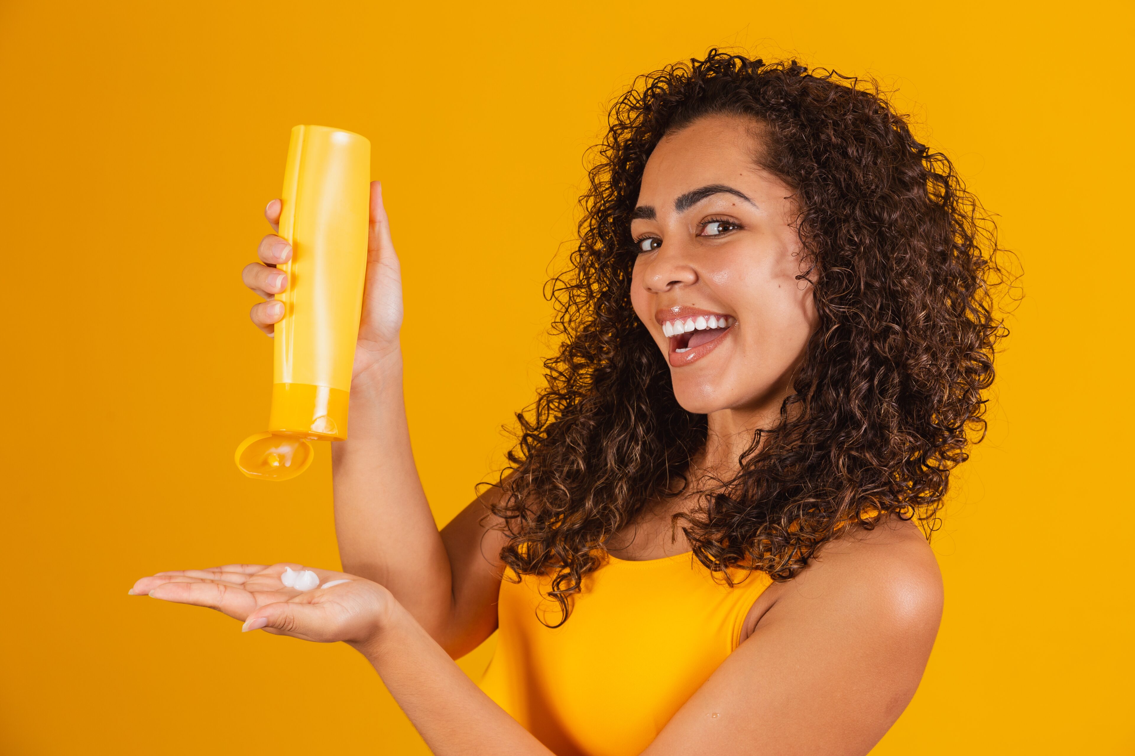 Beautiful woman with curly hair applying cream to her hair