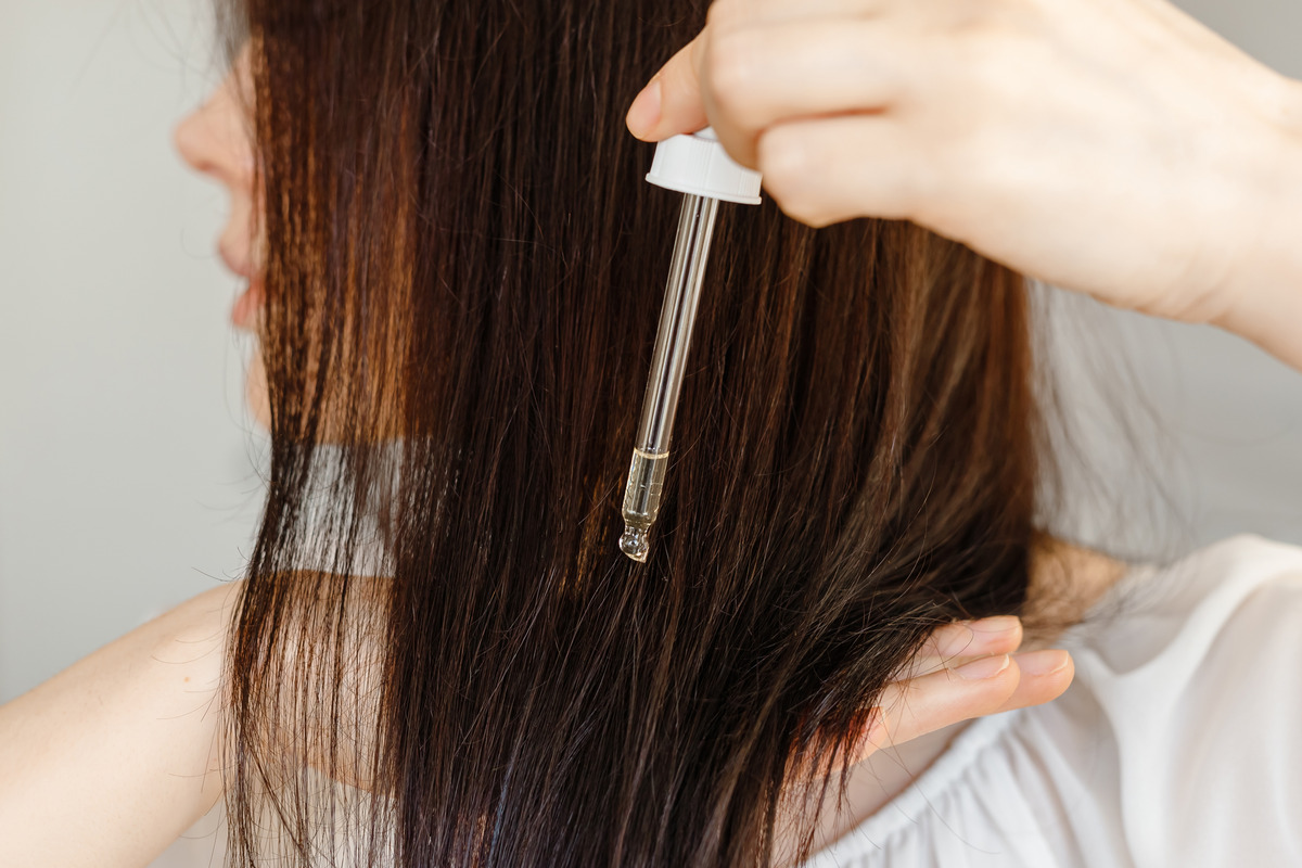 Woman applying dropper with oil or serum essence on ends hair