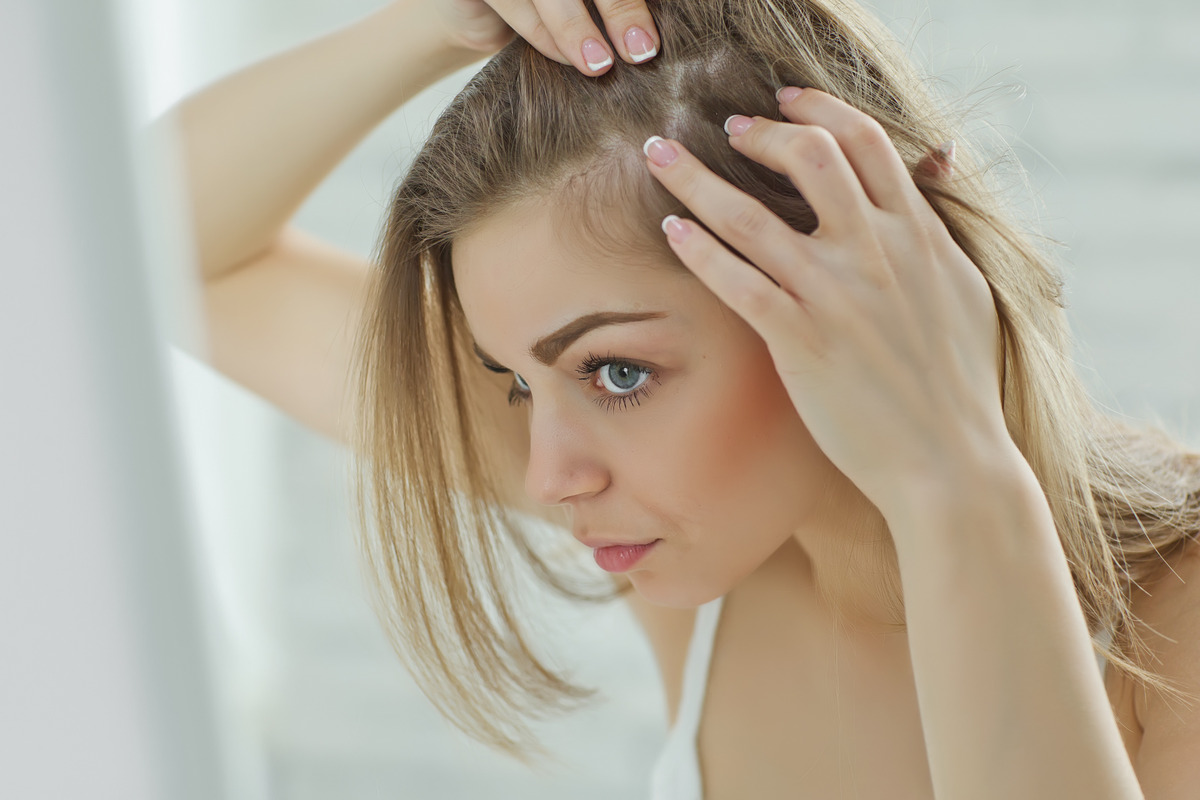 Worried girl looking in the mirror her scalp