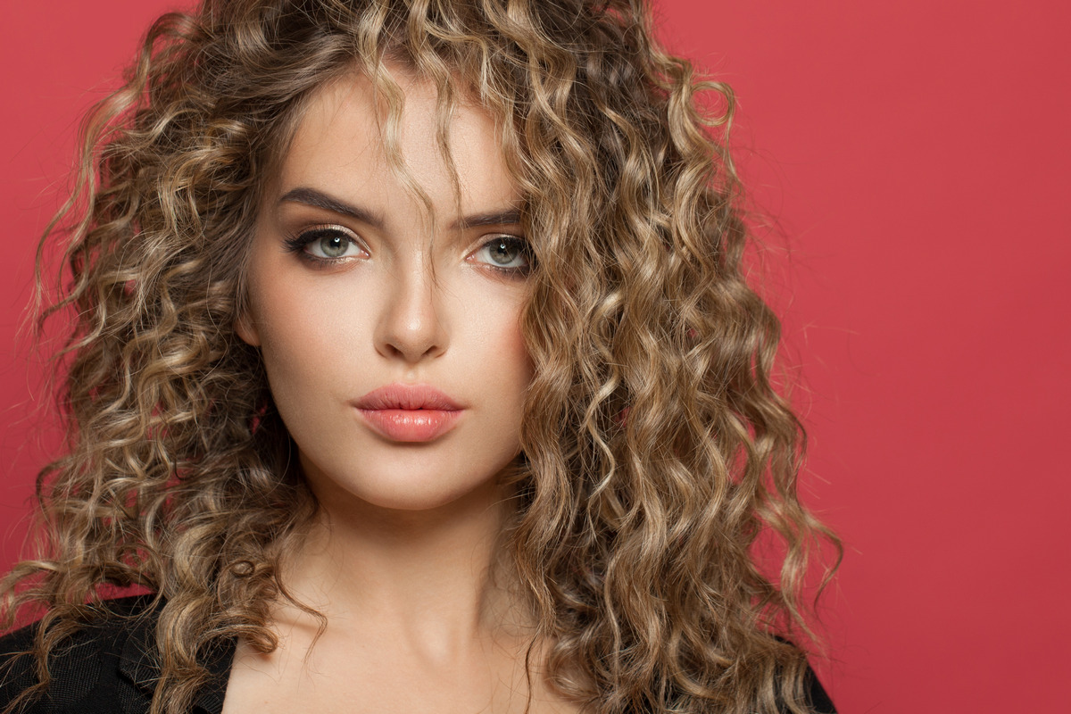 Beautiful woman with curly hair looking at the camera on a red background