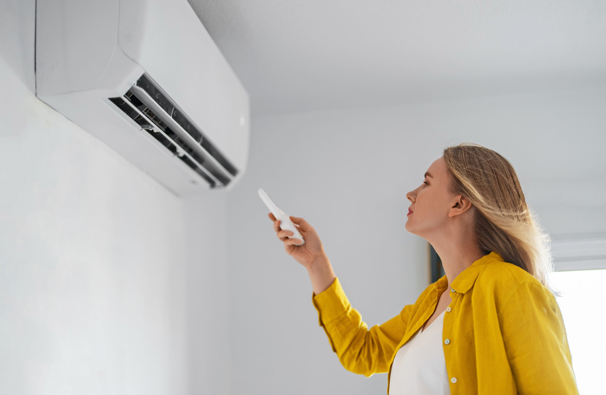 Woman holding remote control aimed at the air conditione