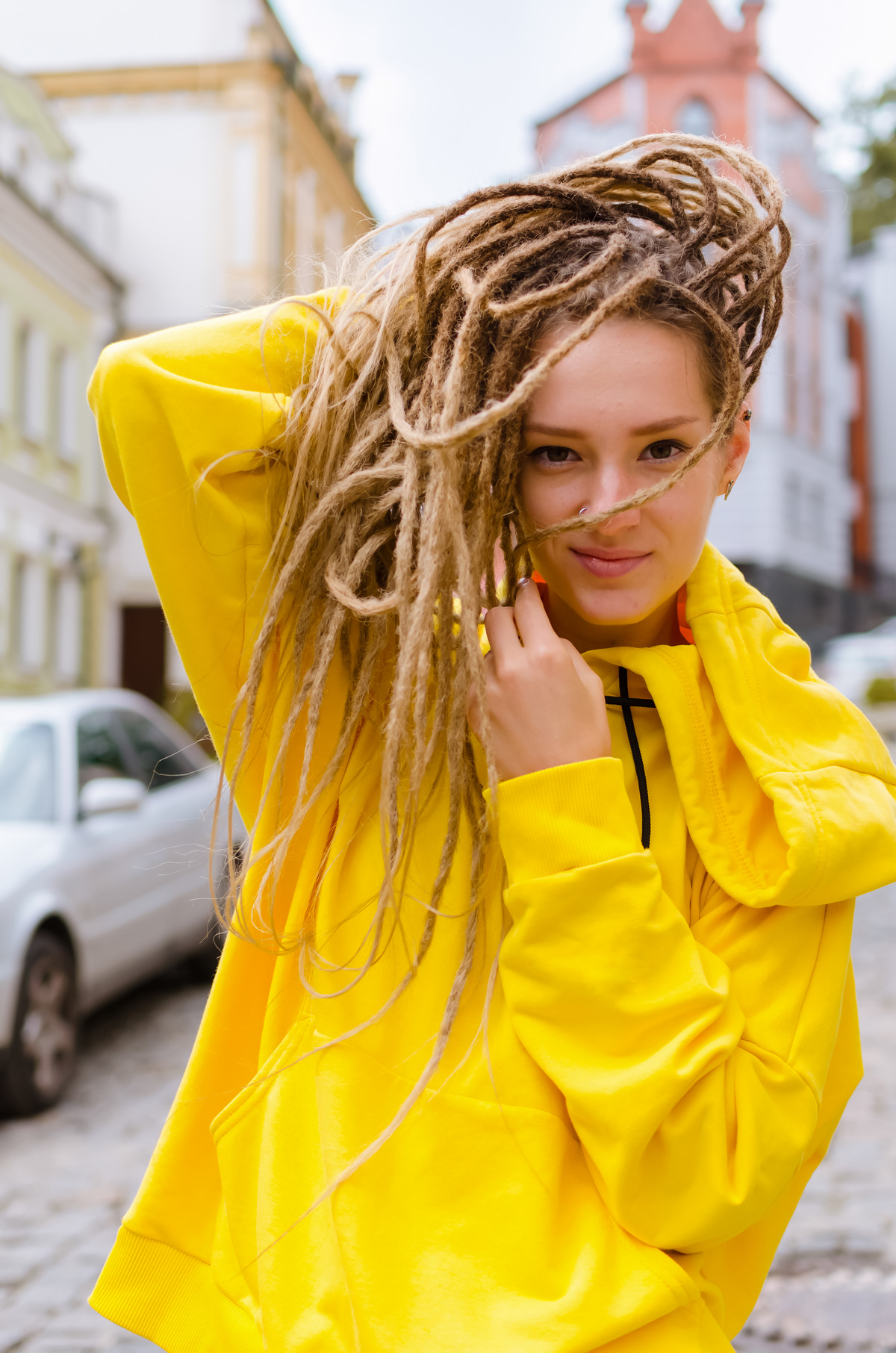Young woman with dreadlocks in a yellow hoodie in the city street